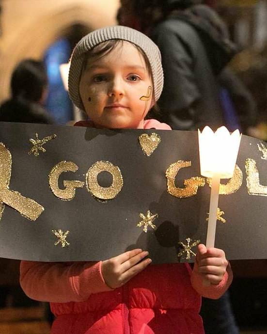 A young child holding a candle and a sign with 'go gold' written on it.