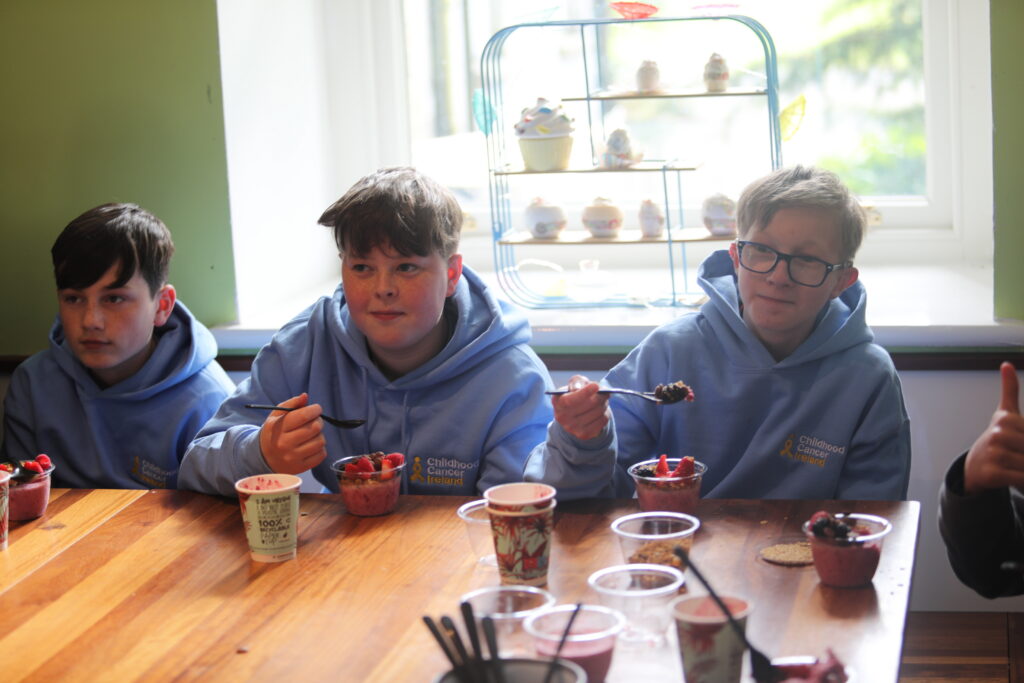 Three young boys sit at a table preparing a snack.